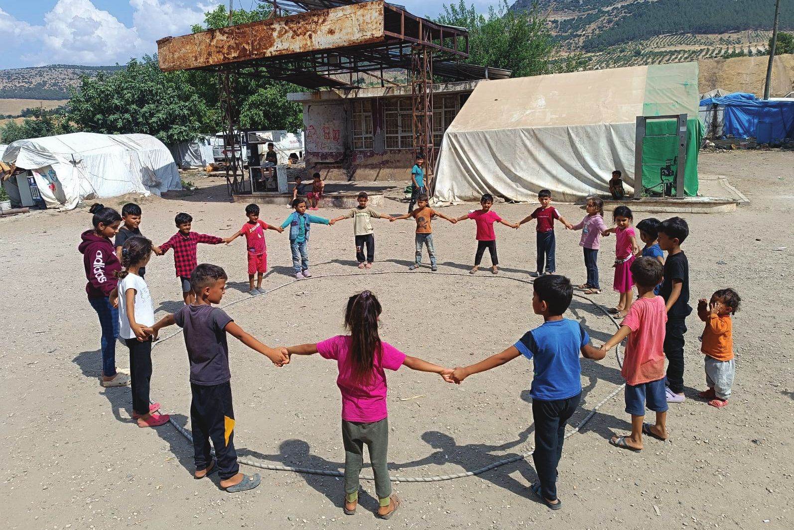 Children playing a circle game in a tent settlement